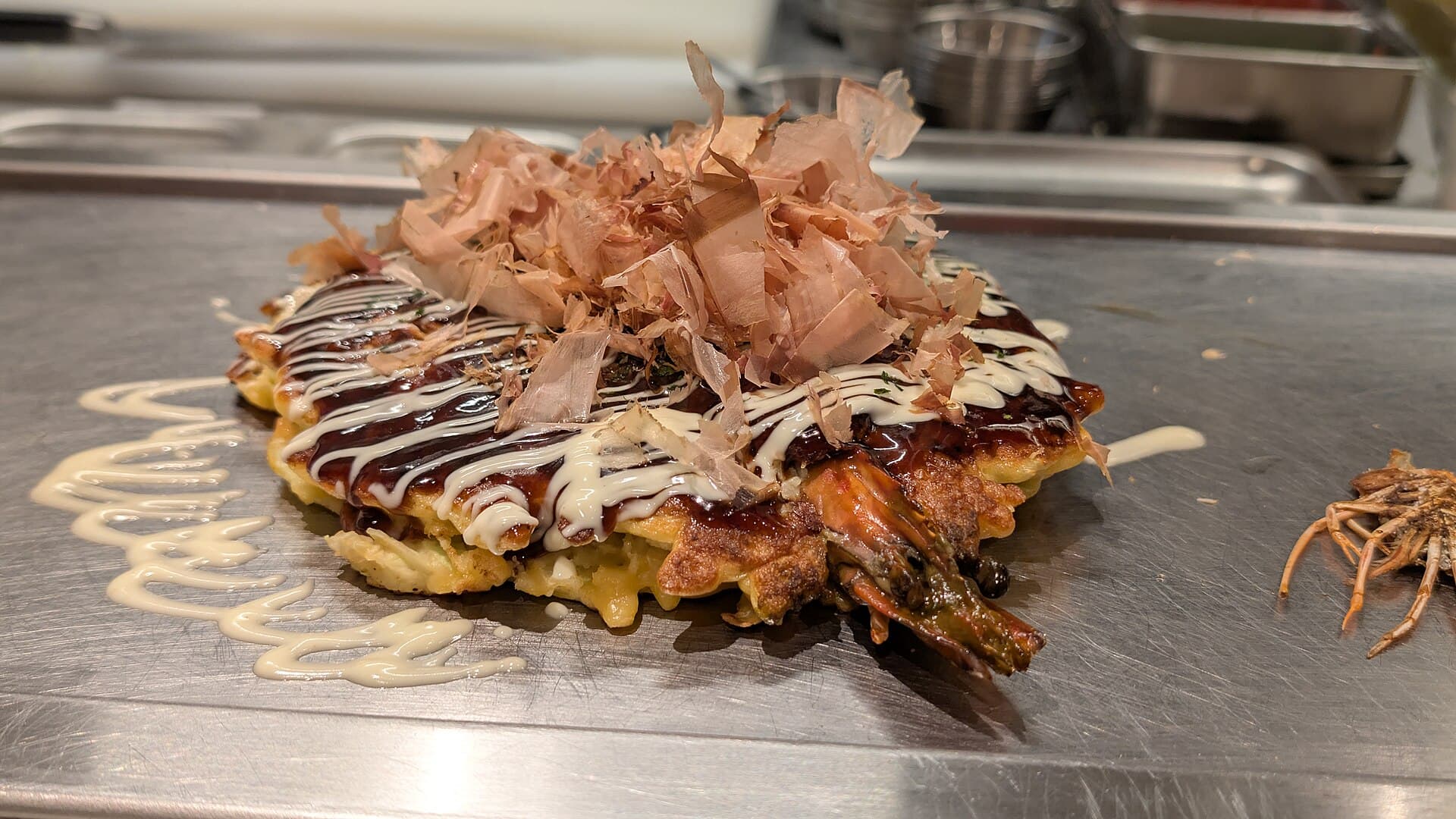Okonomiyaki servi sur une plaque chauffante à Osaka, galette japonaise garnie de sauce et mayonnaise.