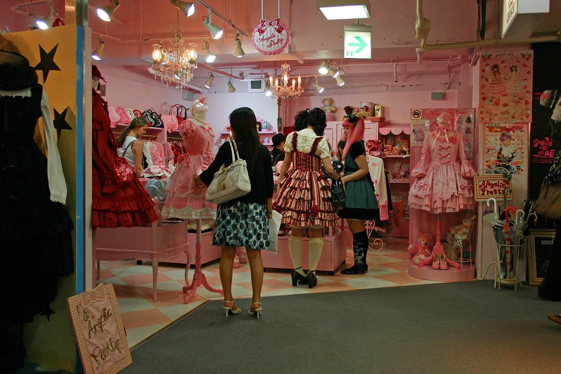 Interieur rose de la boutique Angelic Pretty au Japon : robes Lolita sur presentoirs, clientes en coordination sweet et gothic, chandeliers et sol a damier