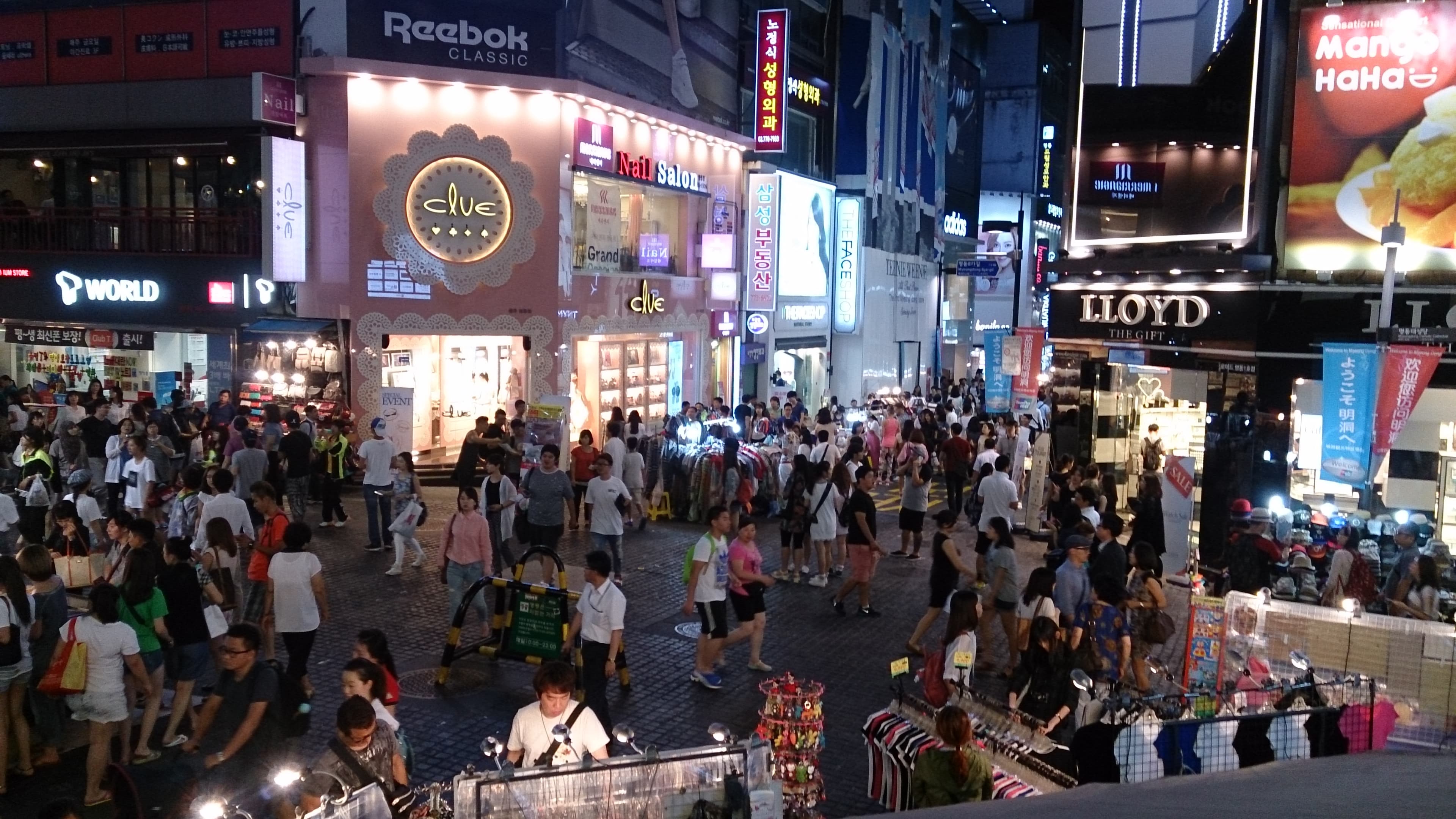 Foule dense de passants dans le quartier commerçant animé de Myeongdong à Séoul, illustrant le rythme rapide de la vie coréenne.