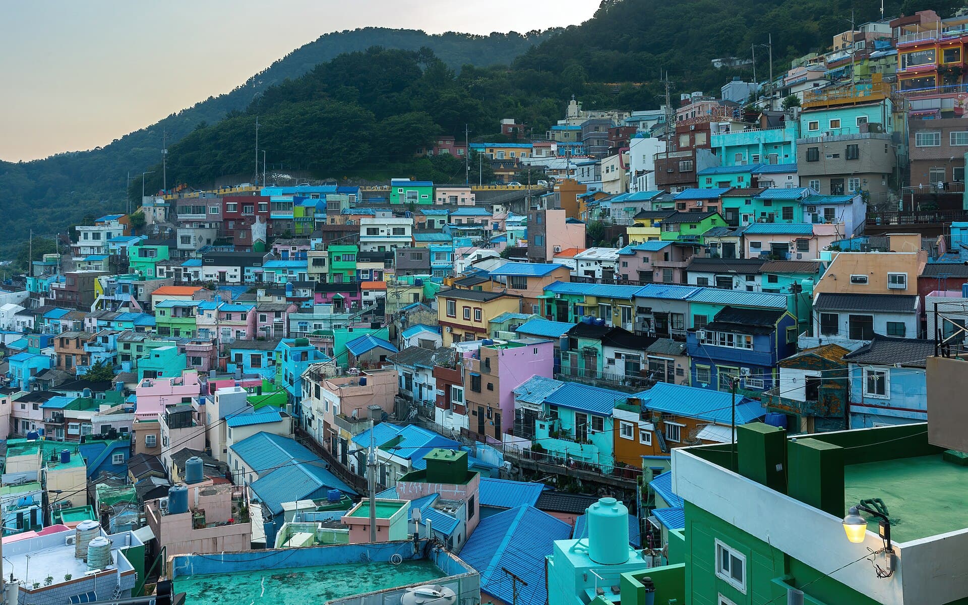 Le village culturel de Gamcheon a Busan au coucher du soleil : des centaines de maisons cubiques peintes en pastel etagees a flanc de colline jusqu'a la mer, reliees par des escaliers et des ruelles etroites