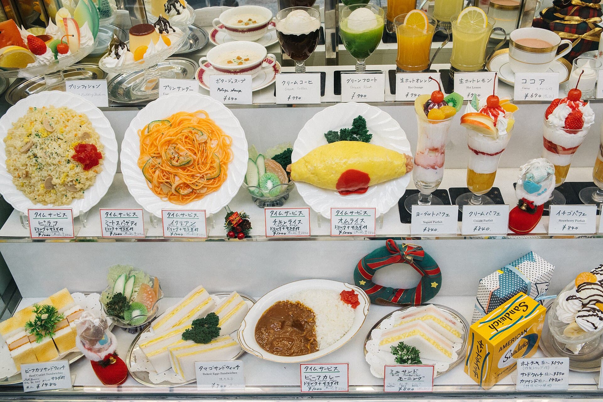 Vitrine de plats en resine du junkissa American a Osaka : naporitan, omurice, cremes soda et parfaits presentes avec leurs etiquettes de prix manuscrites