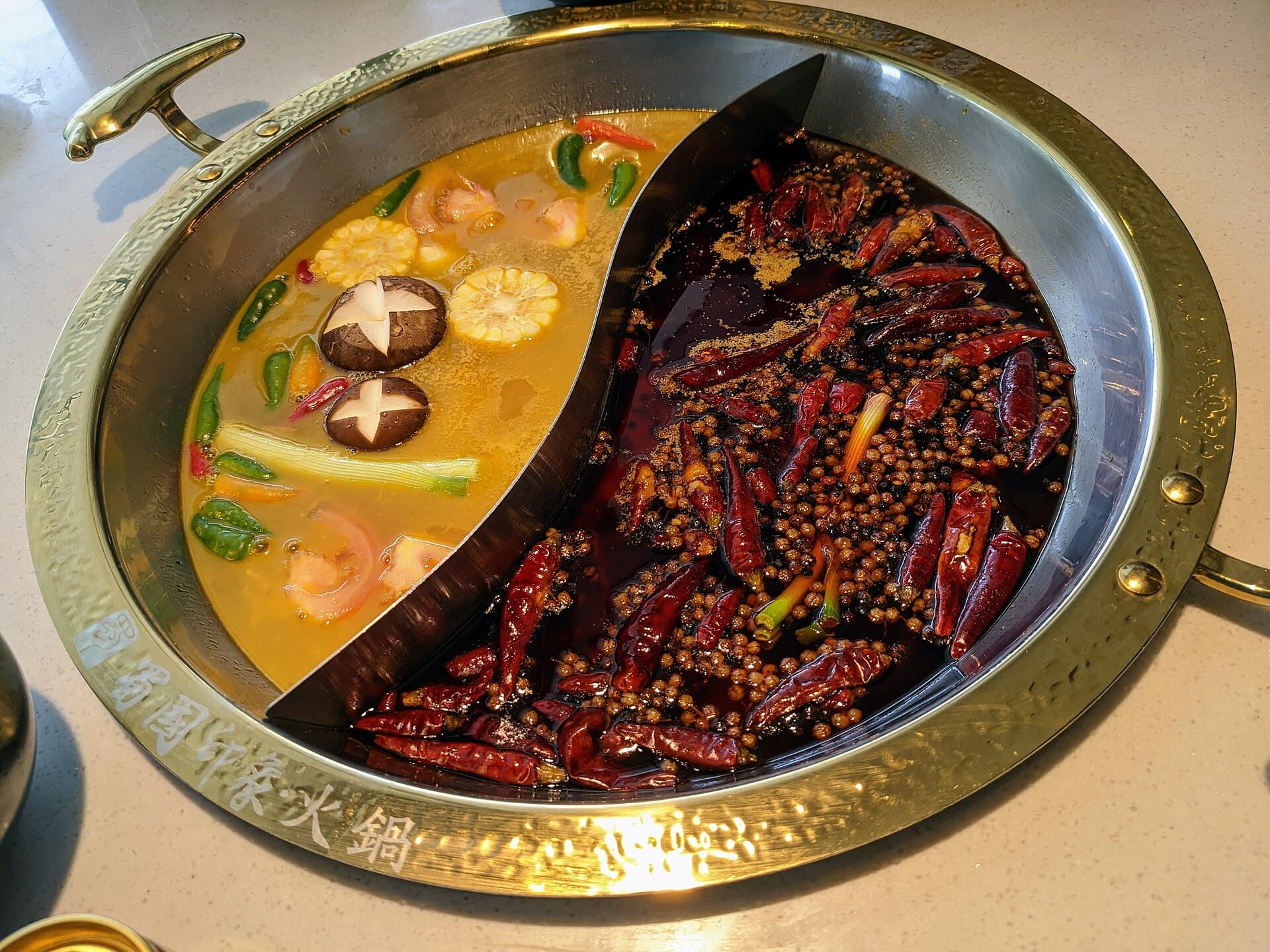 Marmite a hot pot de style Chengdu separee en deux : d'un cote un bouillon clair, de l'autre une huile rouge couverte de piments seches entiers et de baies de poivre du Sichuan