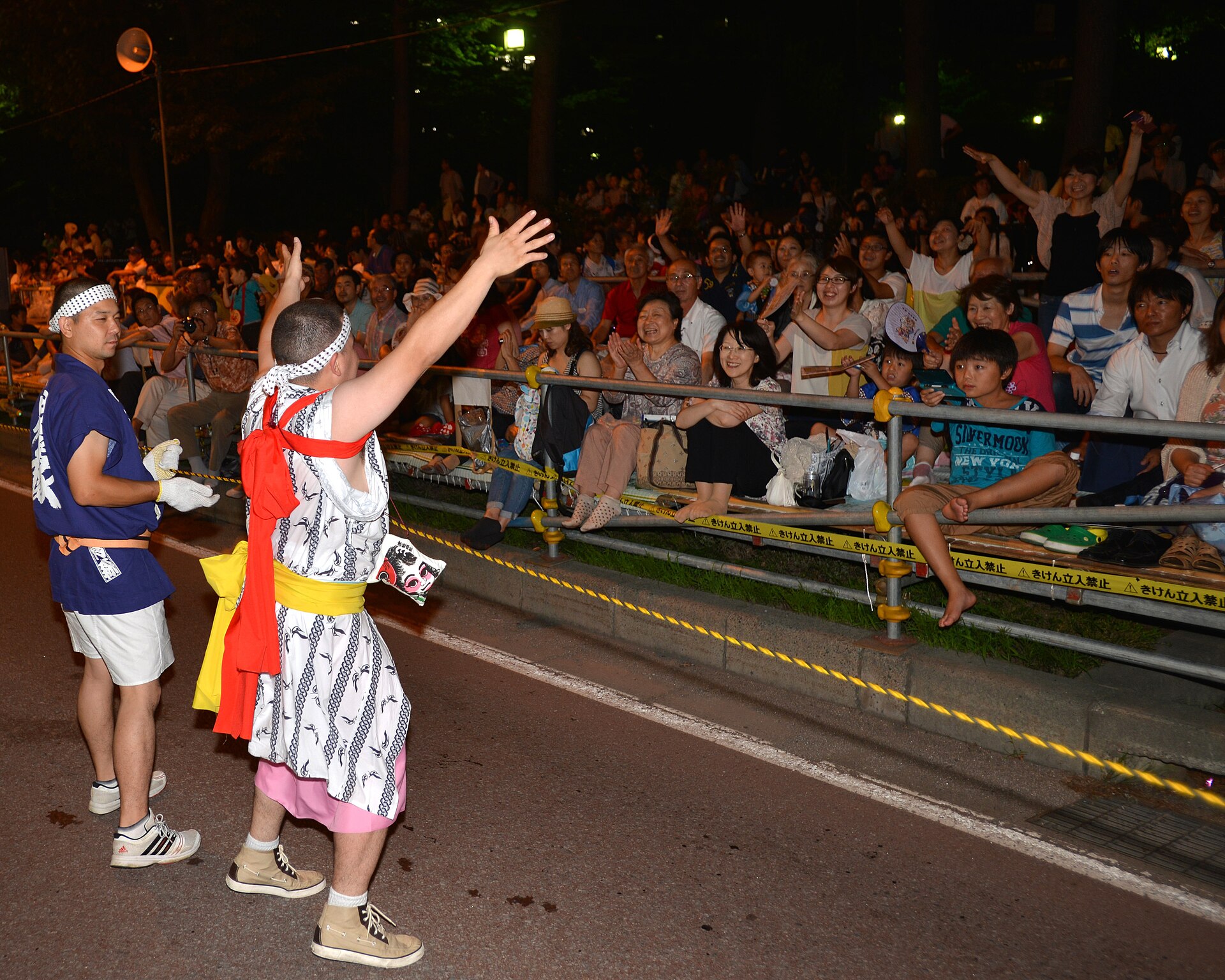 Un bailarín haneto con traje tradicional, sombrero de flores hanagasa y cascabeles, saludando a la multitud durante el desfile nocturno del Nebuta Matsuri de Aomori