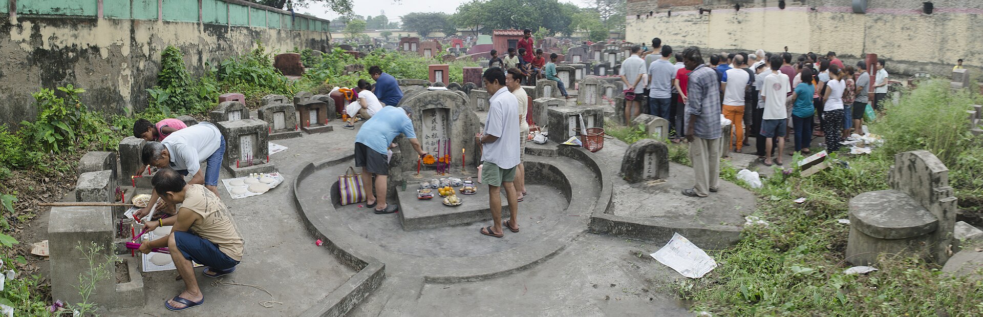A Chinese family cleaning and tending an ancestor's grave on a hillside during the Qingming festival